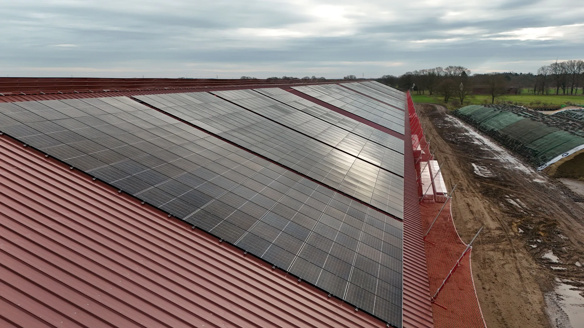 Nahaufnahme der dicht gesetzten Modulreihen auf dem roten Trapezdach vor bewölktem Himmel